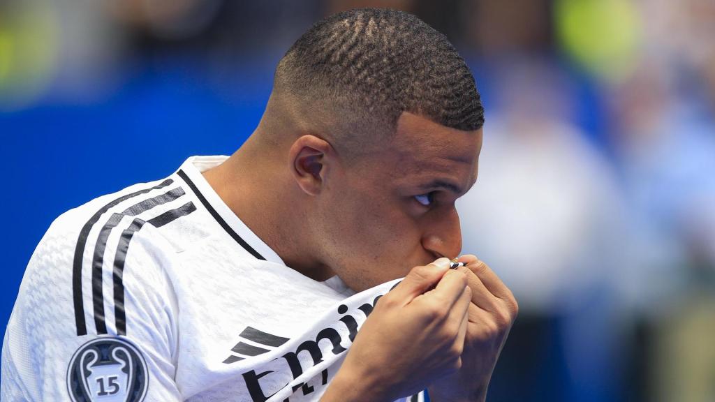 Kylian Mbappé besa el escudo del Real Madrid durante su presentación como nuevo jugador del club, este martes en el estadio Santiago Bernabéu de Madrid.