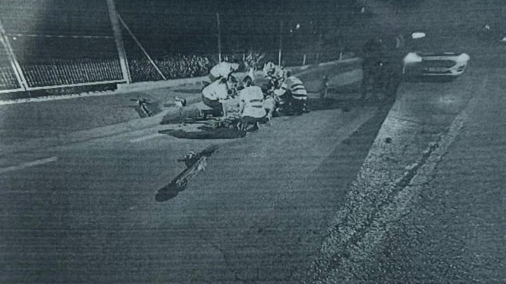 En primer plano, el patinete eléctrico de los dos menores de edad, completamente destrozado. Al fondo, unos sanitarios reanimando a Iván y Sonia sobre el asfalto.