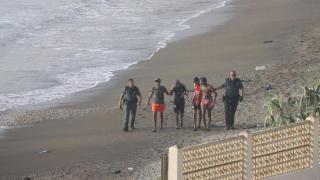 Dos guardias civiles escoltan a cuatro jóvenes migrantes llegados a nado a la playa del tarajal en Ceuta.