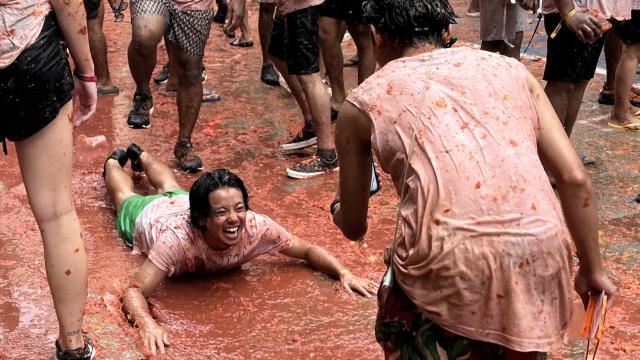 Dos visitantes inmortalizan el momento en el que uno se lanza al charco de tomate en Buñol (Valencia). Raquel Granell