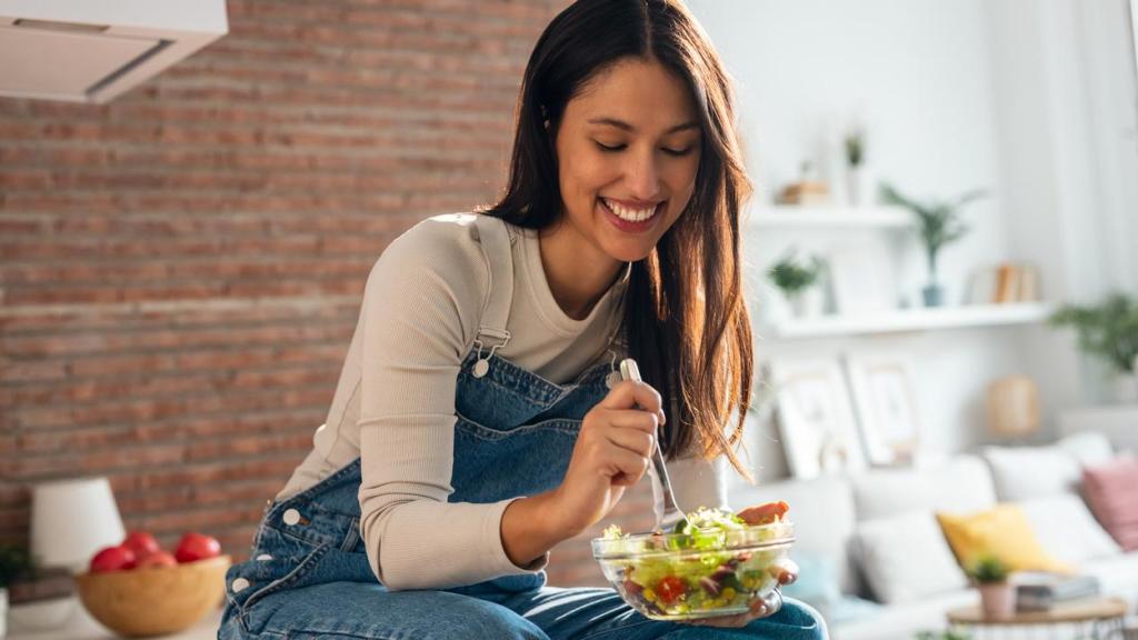 Mujer comiendo una ensalada sobre la encimera de la cocina.