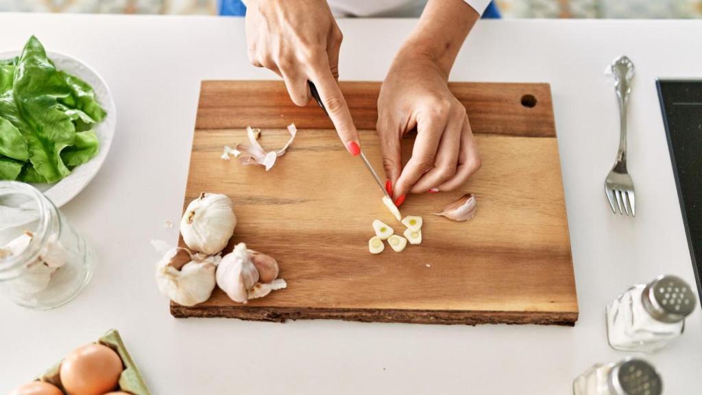 Mujer troceando ajos sobre una tabla de cortar.