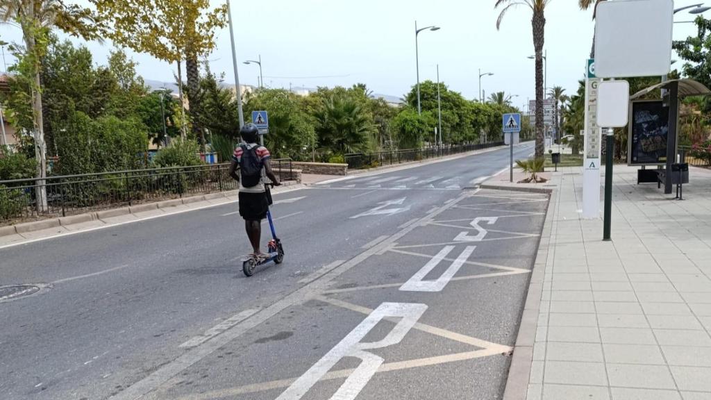 Un joven de ascendencia africana circula con un patinete eléctrico por la calle principal de Vícar.
