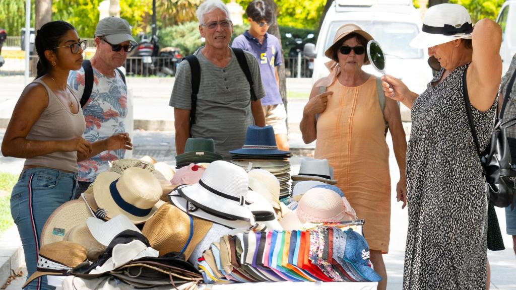 Un grupo de turistas compra gorros para protegerse del sol en Sevilla.