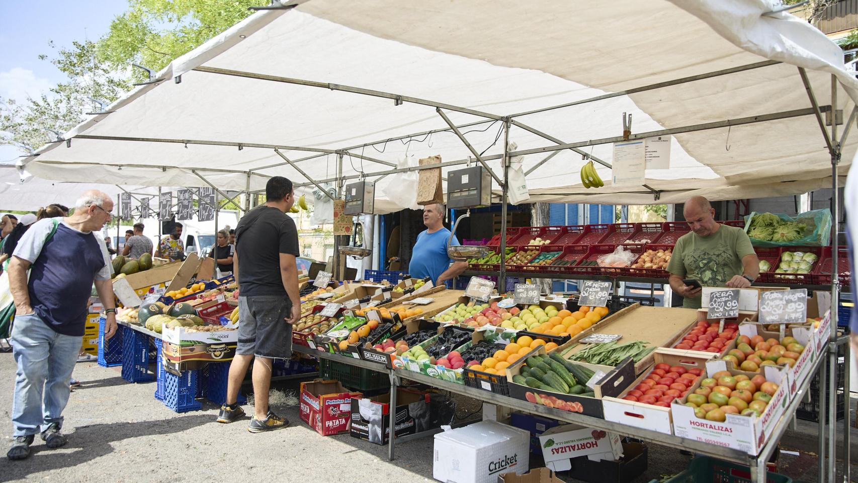 Varias personas compran en un puesto de frutas en el mercadillo de Plaza Elíptica, en Madrid (España).