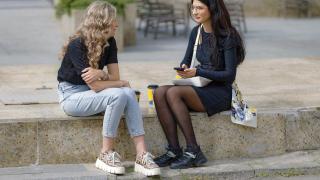 Dos jóvenes hablando sentadas en la calle.