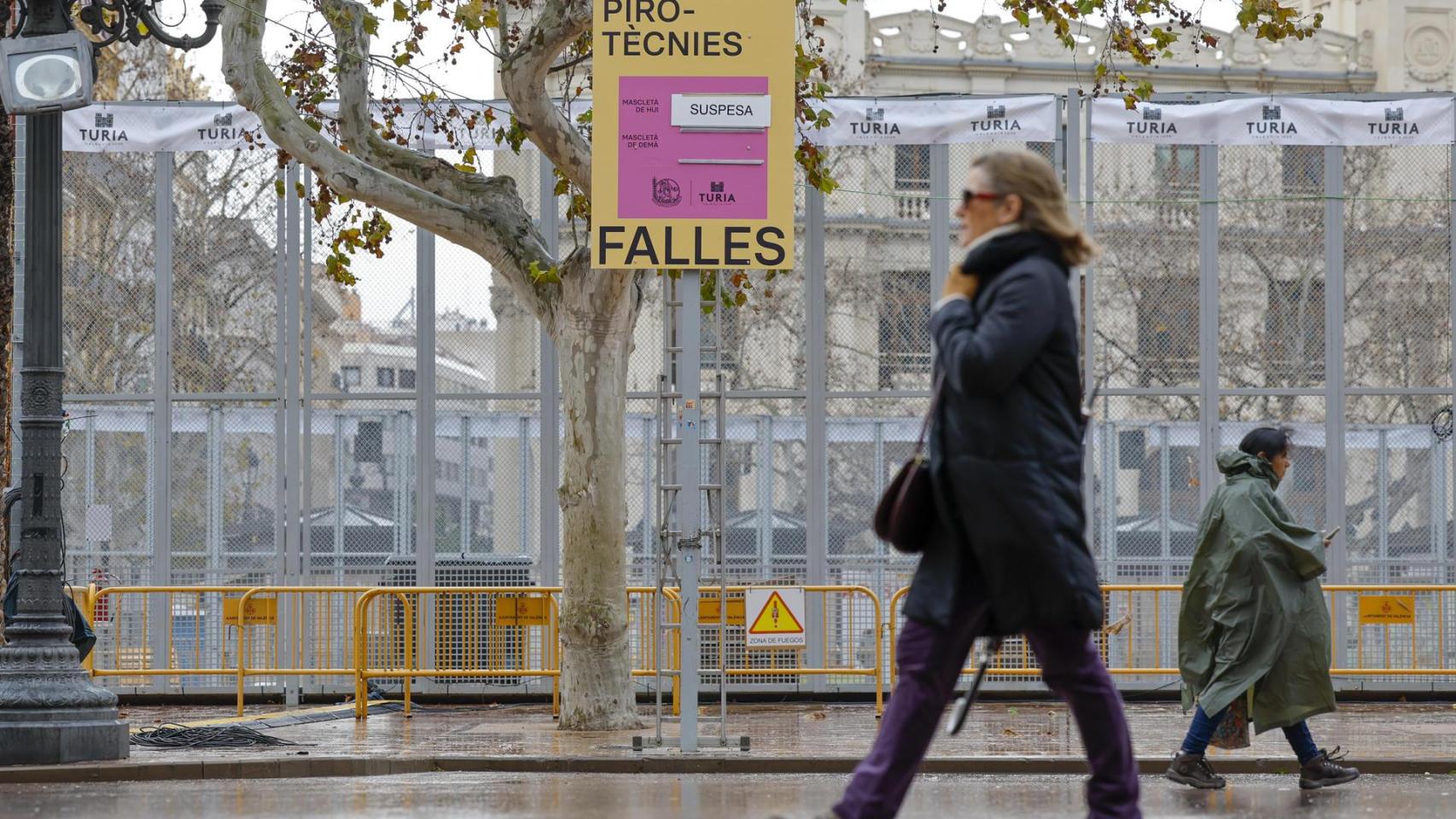 Dos personas pasan ante el cartel que anuncia la suspensión de las 'mascletàs' durante ante la Emergencia por inundaciones. Efe / Ana Escobar