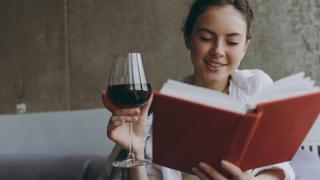 Mujer bebiendo vino tinto mientras lee.