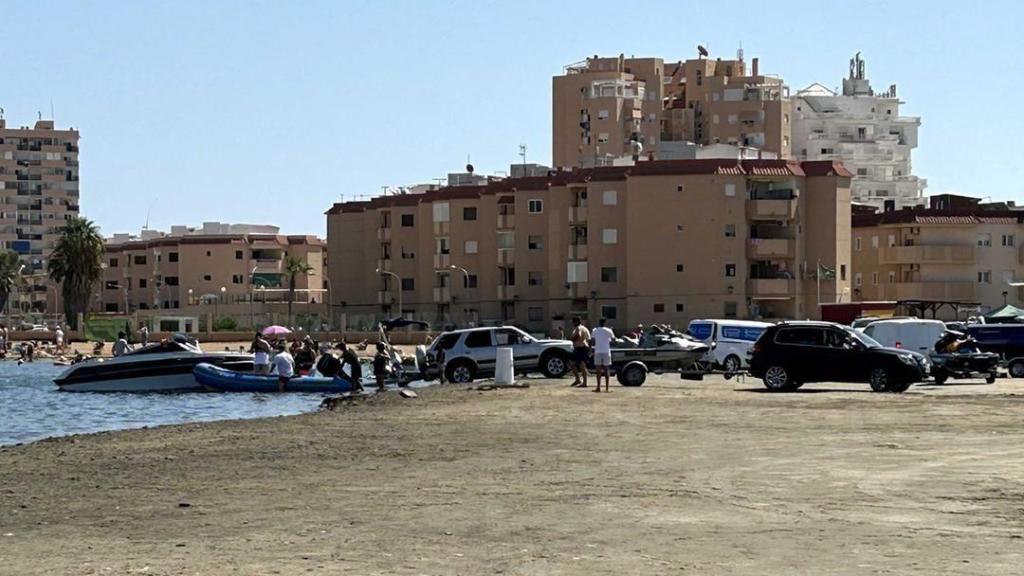 Un grupo de personas introduce sus coches en la arena de una playa del Mar Menor, para acceder a sus embarcaciones.