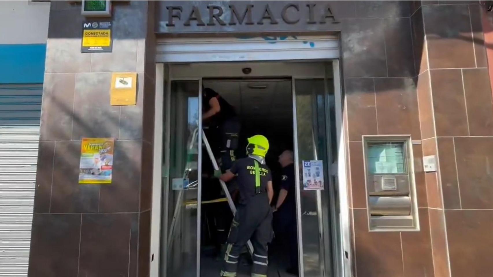 Bomberos de Sevilla trabajan para cerrar la persiana automática de una farmacia.