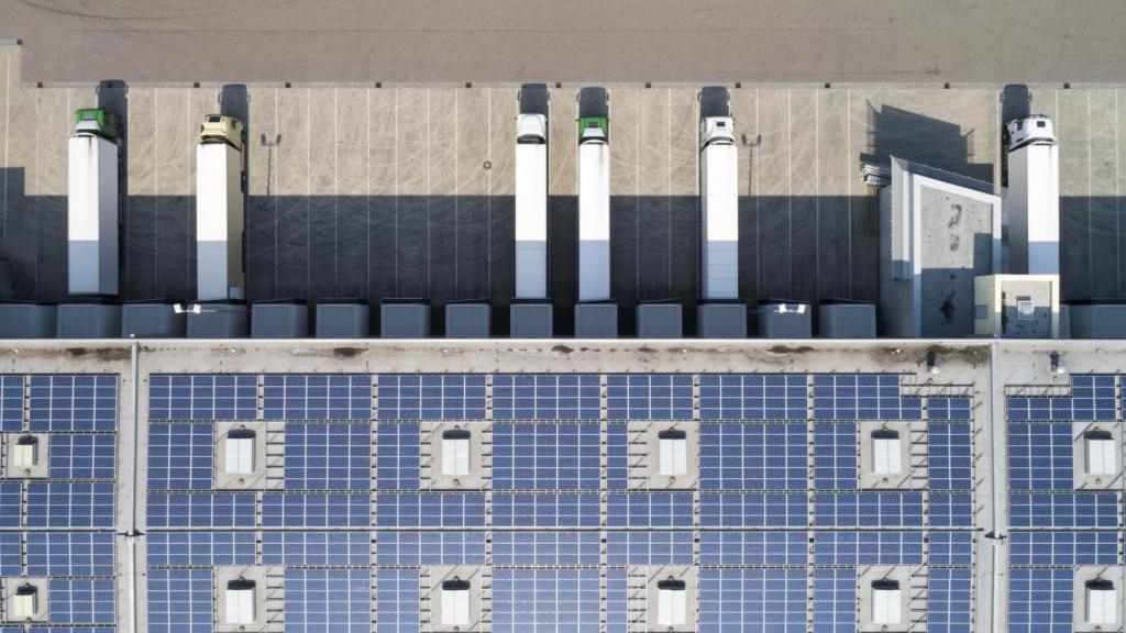 Vista panorámica de camiones descargando en un polígono industrial con techos solares.