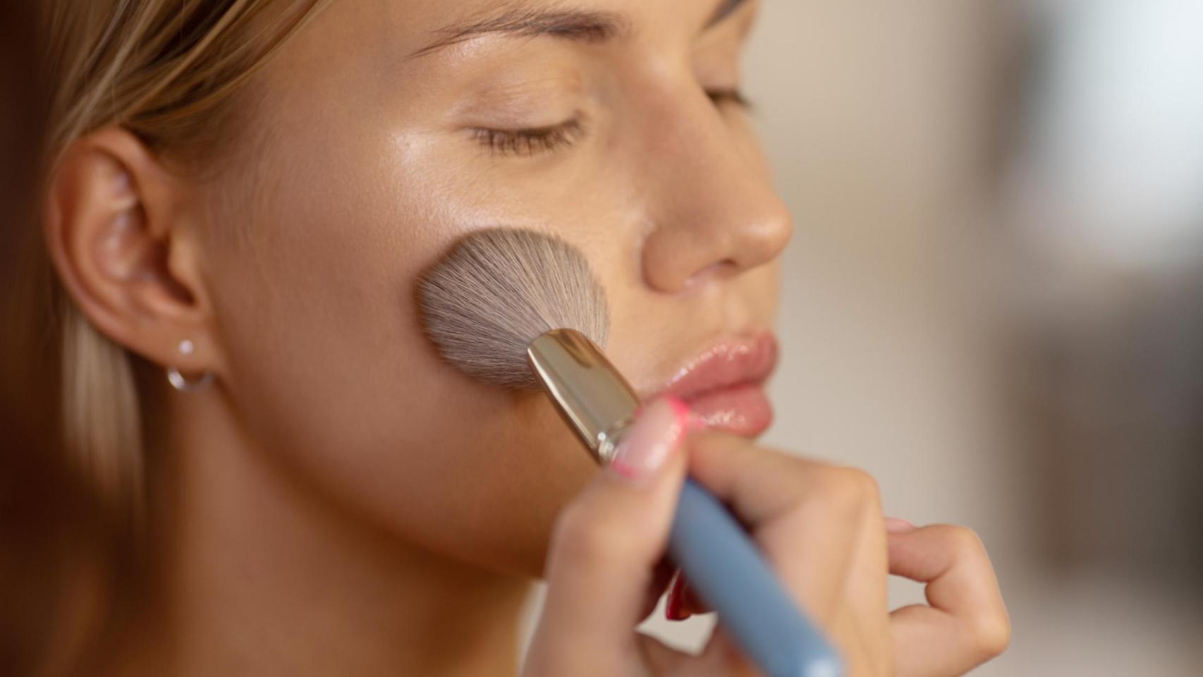 Mujer aplicándose maquillaje con una brocha.