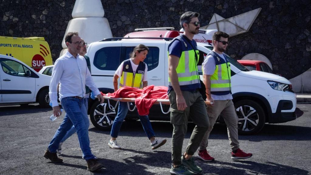Agentes de Policía Nacional y Guardia Civil llevan en la camilla a uno de los migrantes que viajaban en el cayuco que volcó en su llegada al puerto de La Restinga.