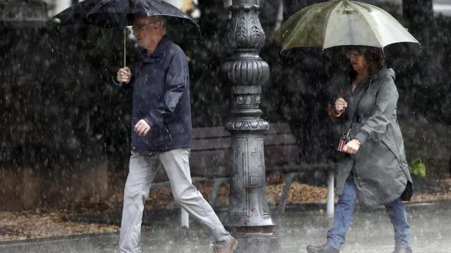 Dos personas se resguardan con sus paraguas de la lluvia.