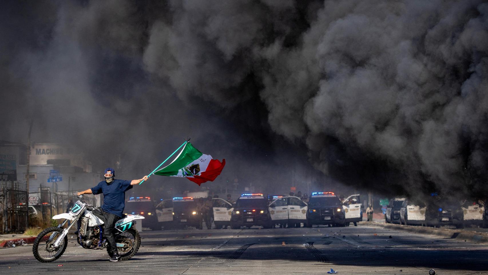 Un manifestante enarbola la bandera mexicana frente a una línea de policías durante las protestas contra las redadas del Servicio de Inmigración y Control de Aduanas (ICE) en Los Ángeles.