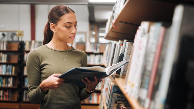 Una mujer cogiendo un libro en una biblioteca, en una imagen de Shutterstock.