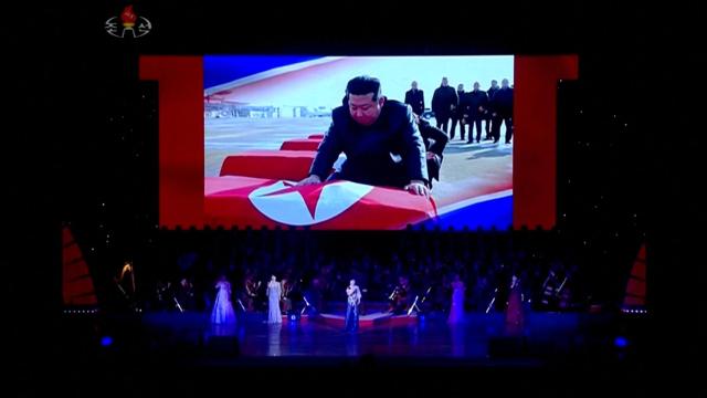 Artistas sobre el escenario mientras se proyecta en una pantalla la imagen de Kim Jong-un cubriendo ataúdes con la bandera norcoreana, en Pyongyang, Corea del Norte, el 29 de junio de 2025, en esta imagen tomada de un vídeo.
