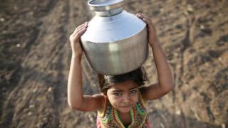 Una niña lleva una jarra de metal llena de agua por un campo en Latur, India. Existe un déficit de inversión anual de 4 billones de dólares para alcanzar los Objetivos de Desarrollo Sostenible de la ONU para 2030.