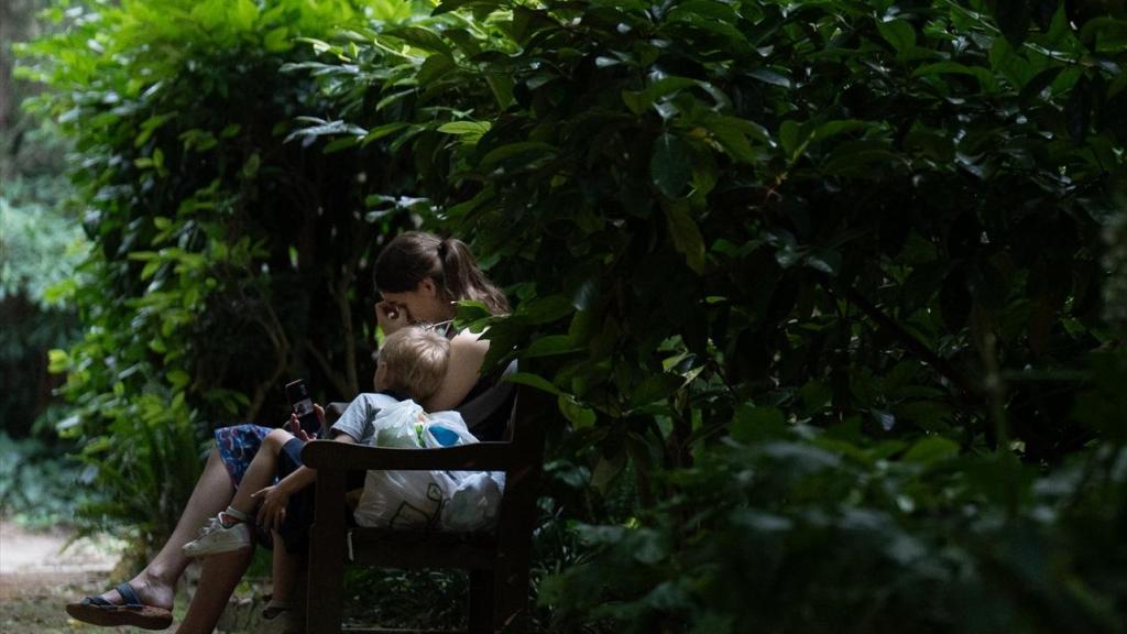 Dos personas sentadas en el banco de un parque de Barcelona que hace las funciones de refugio climático durante las olas de calor.