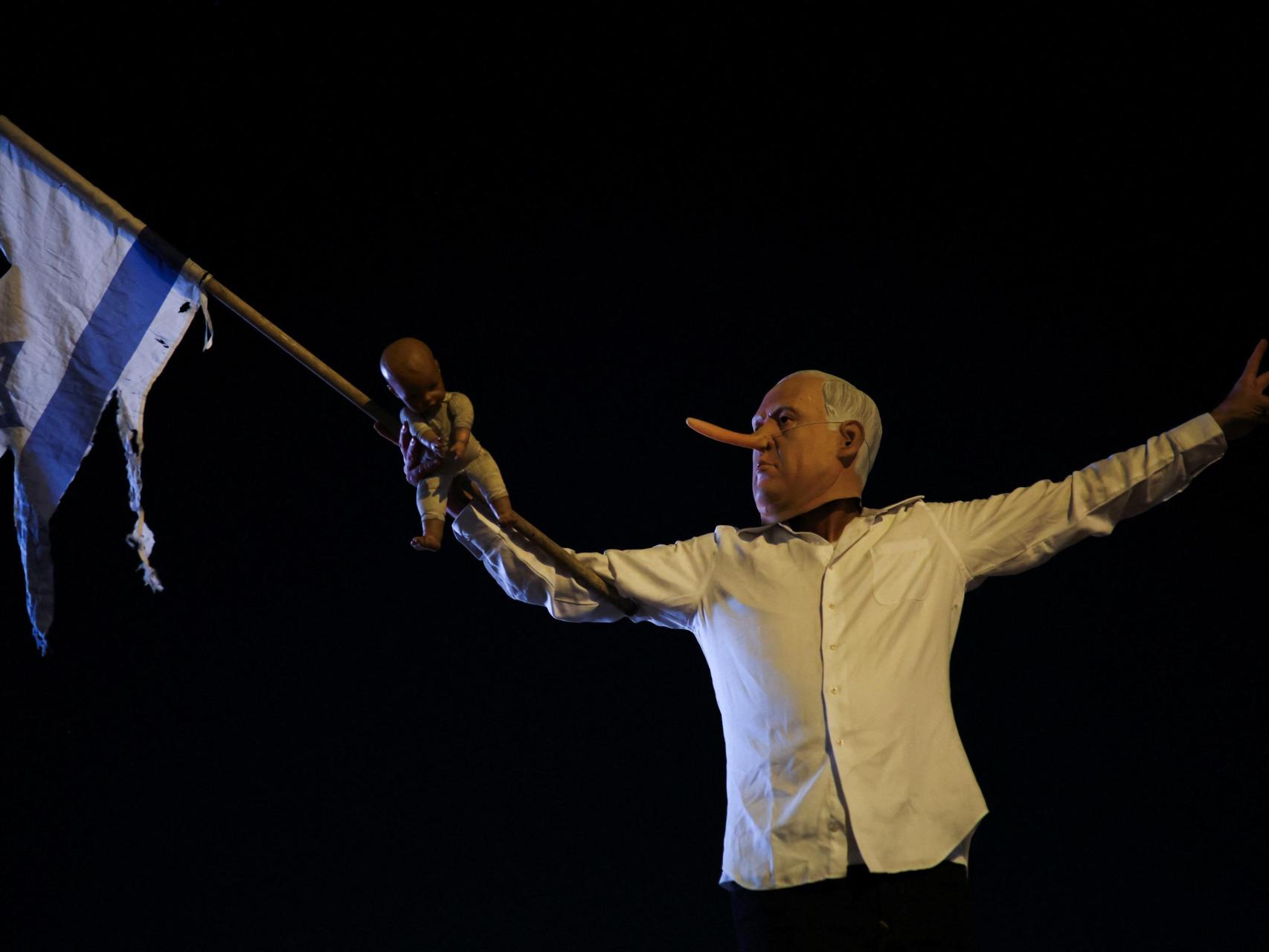 Un manifestante con una nariz postiza y una máscara del primer ministro israelí Benjamin Netanyahu sostiene un muñeco y una bandera israelí rasgada mientras participa en una protesta para exigir el fin de la guerra en Gaza.