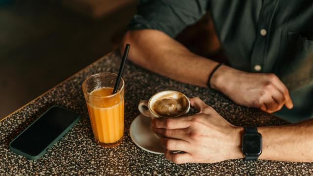 Un hombre tomando un café capuchino y un zumo de naranja en una cafetería.