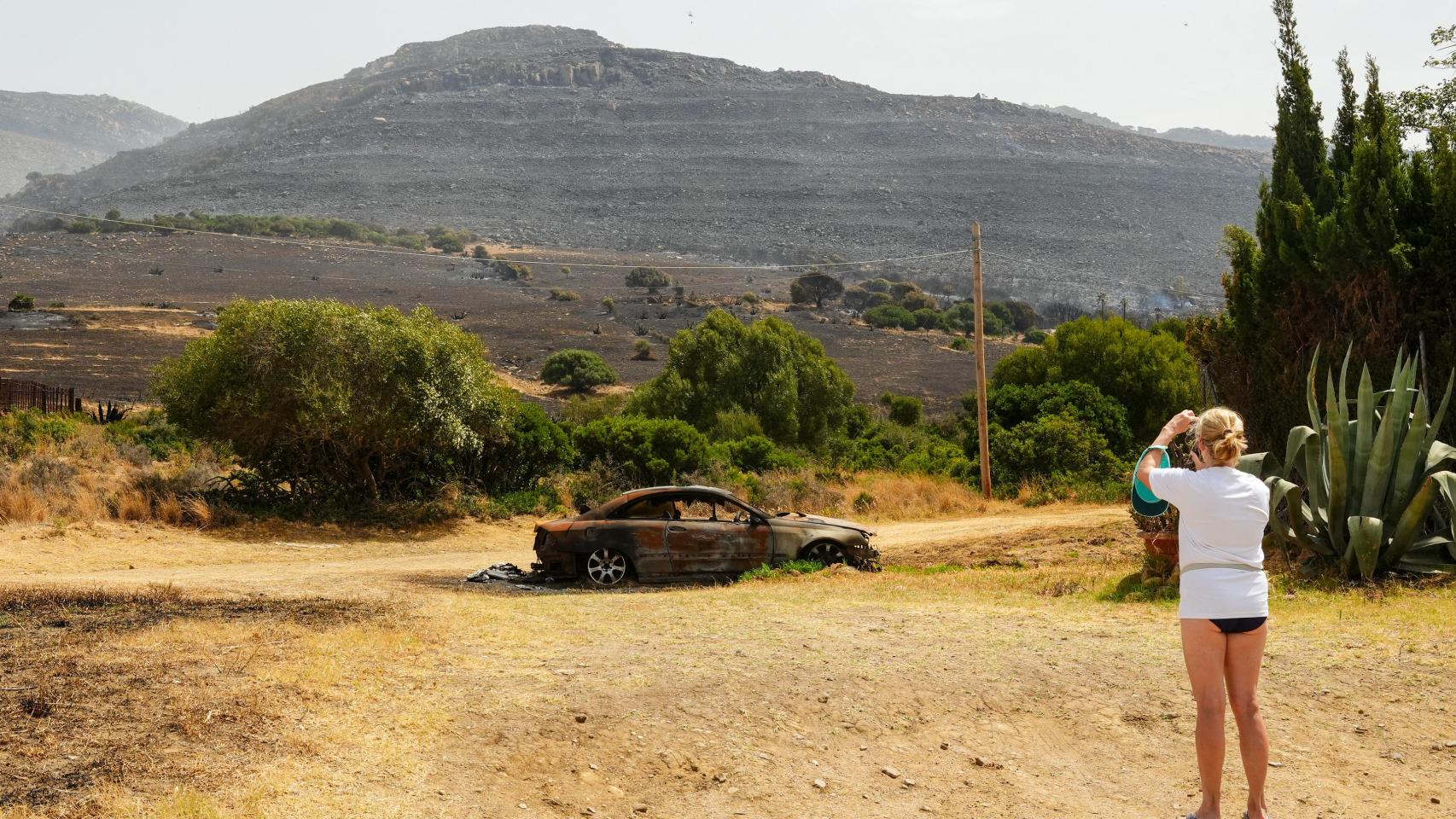 Una mujer observa un coche calcinado tras el incendio de Tarifa.