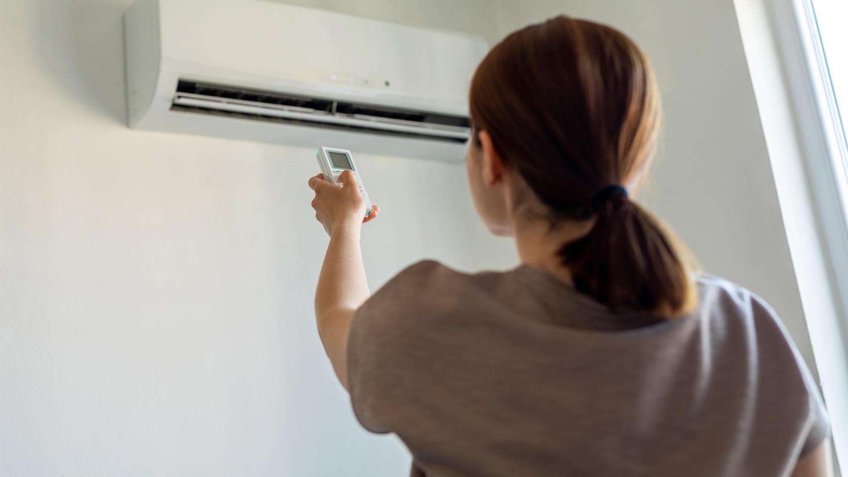 Imagen de recurso de una mujer encendiendo un aire acondicionado.