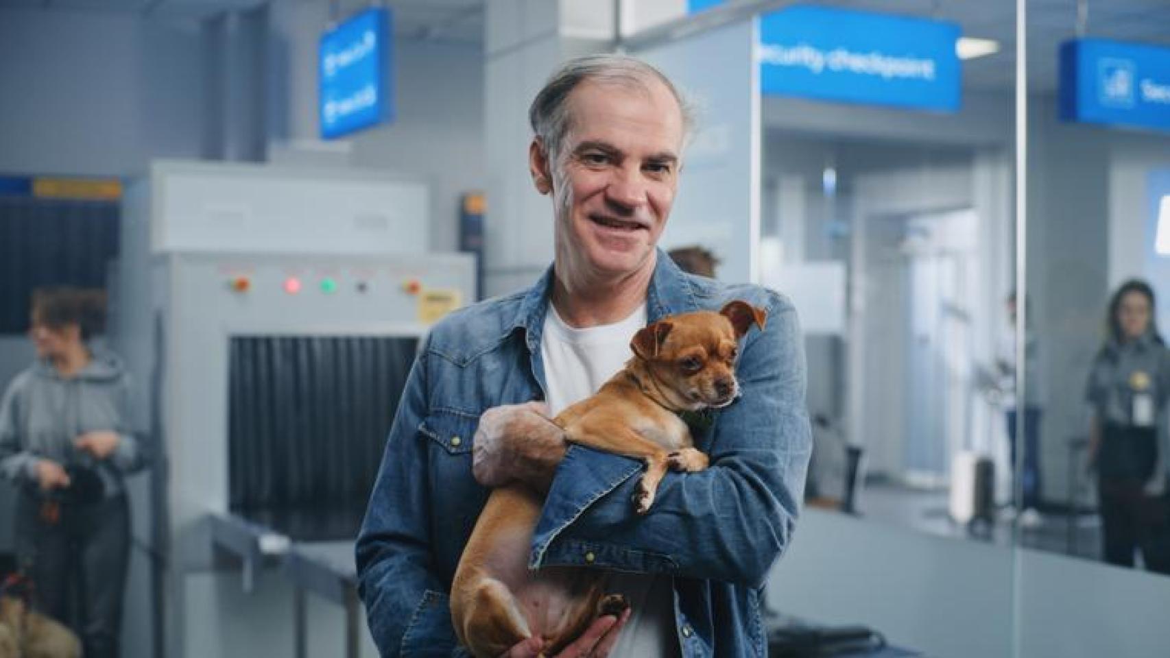 Un hombre con un perro en brazos en un aeropuerto.