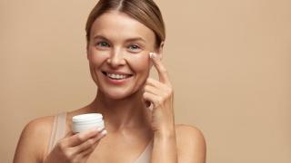 Mujer aplicándose crema en el contorno de ojos.