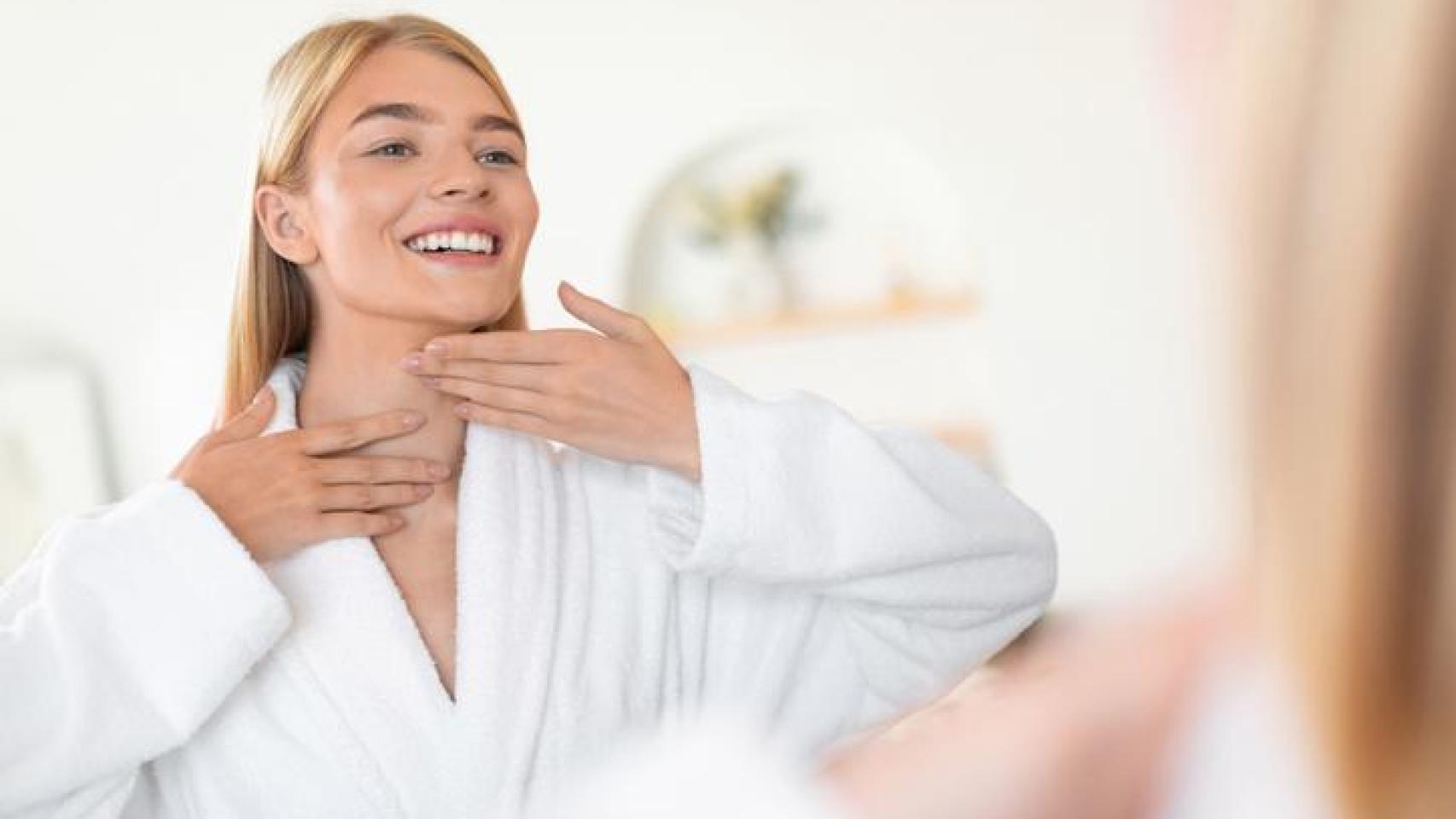 Mujer frente al espejo aplicándose crema en el rostro y cuello.
