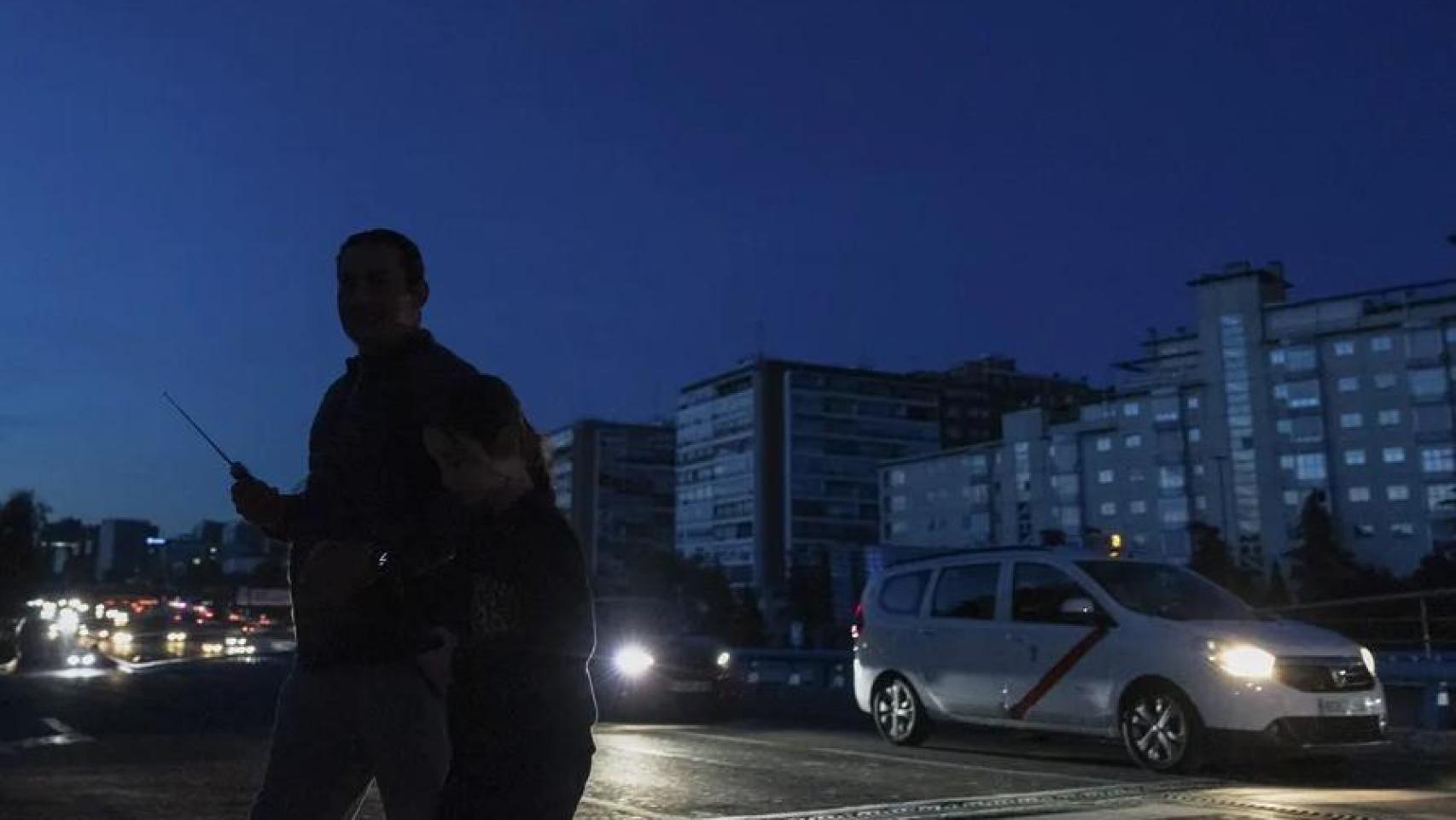 Dos personas cruzando una calle en Madrid a oscuras.