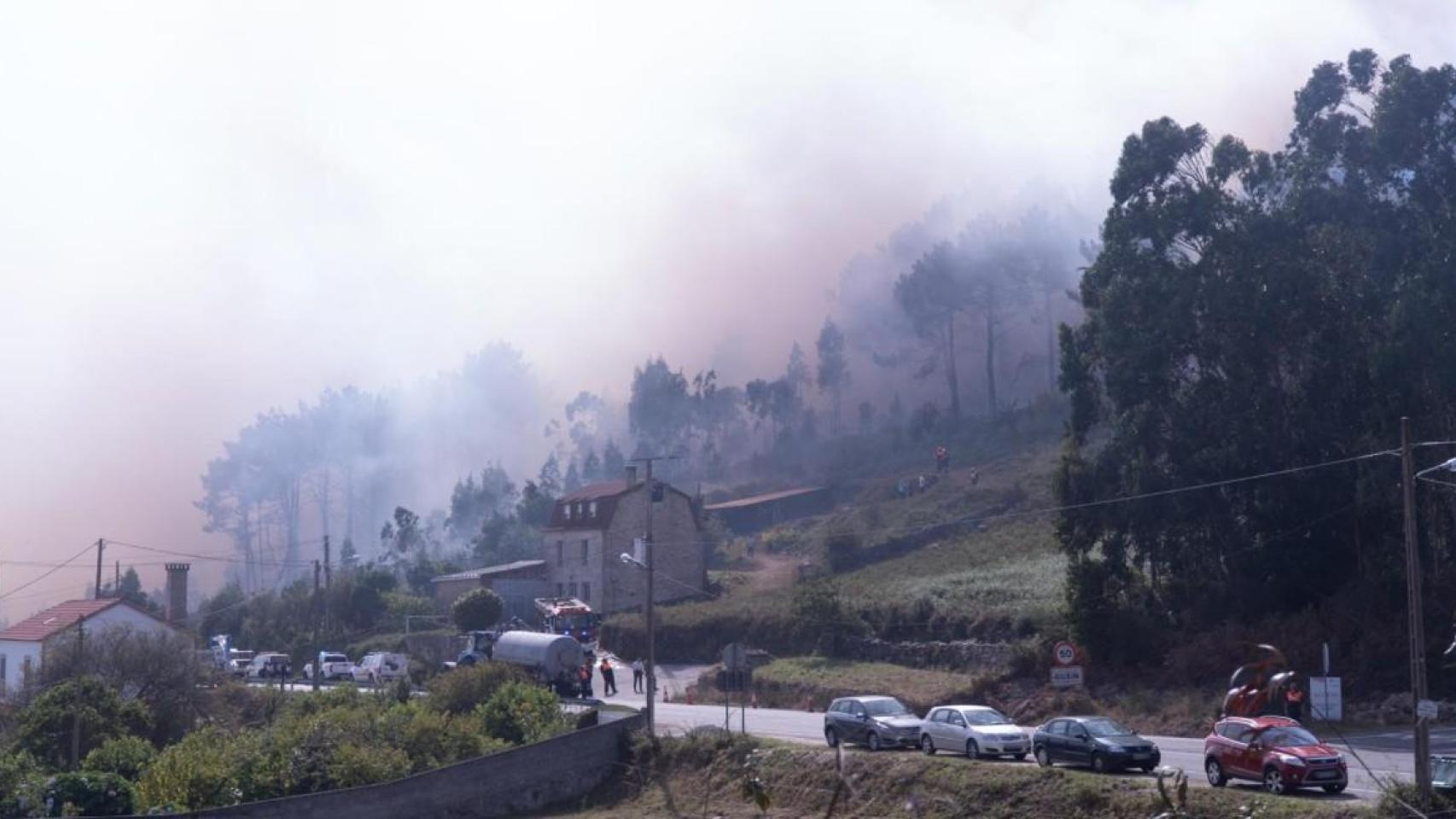 Vehículos circulan por una carretera gallega con un fuego activo durante la ola de incendios.