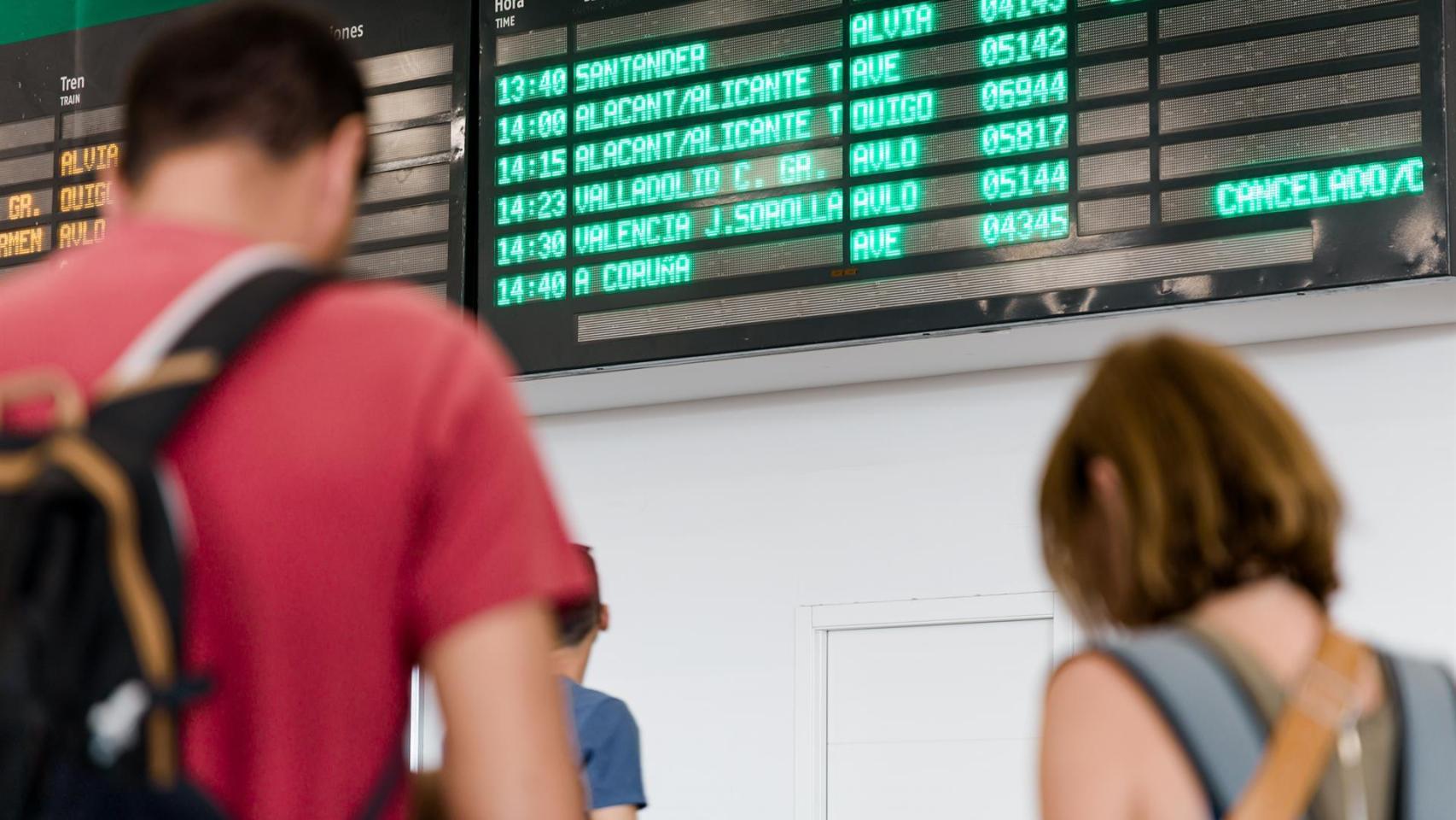 Varias personas esperan con maletas, junto a los carteles de salidas, en la estación Chamartín Clara Campoamor, a 19 de agosto de 2025, en Madrid
