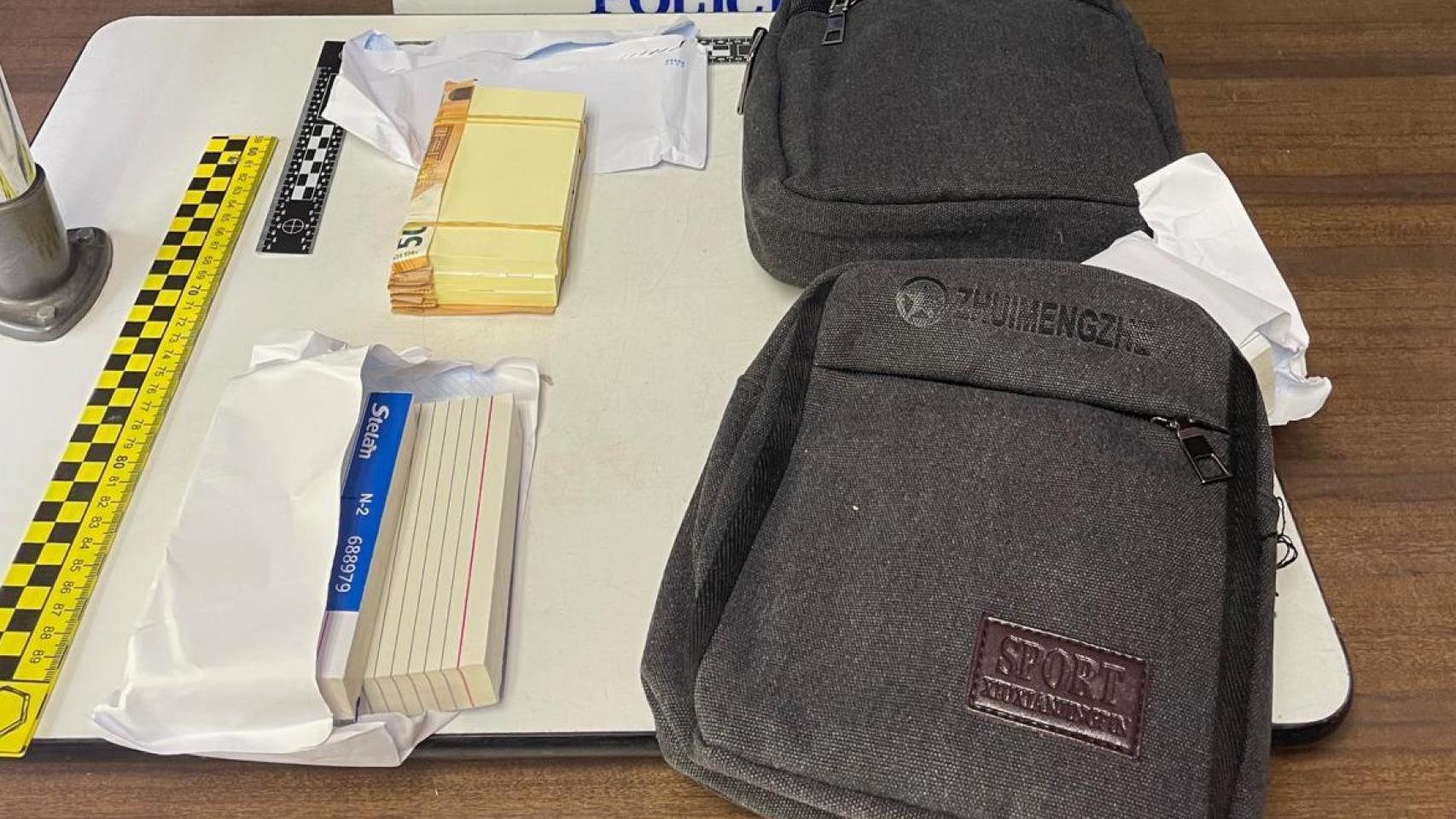 Dos bolsas de mano con varios billetes falsamente presentados como dinero real, disimulando entre papeles para aparentar un fajo legítimo.