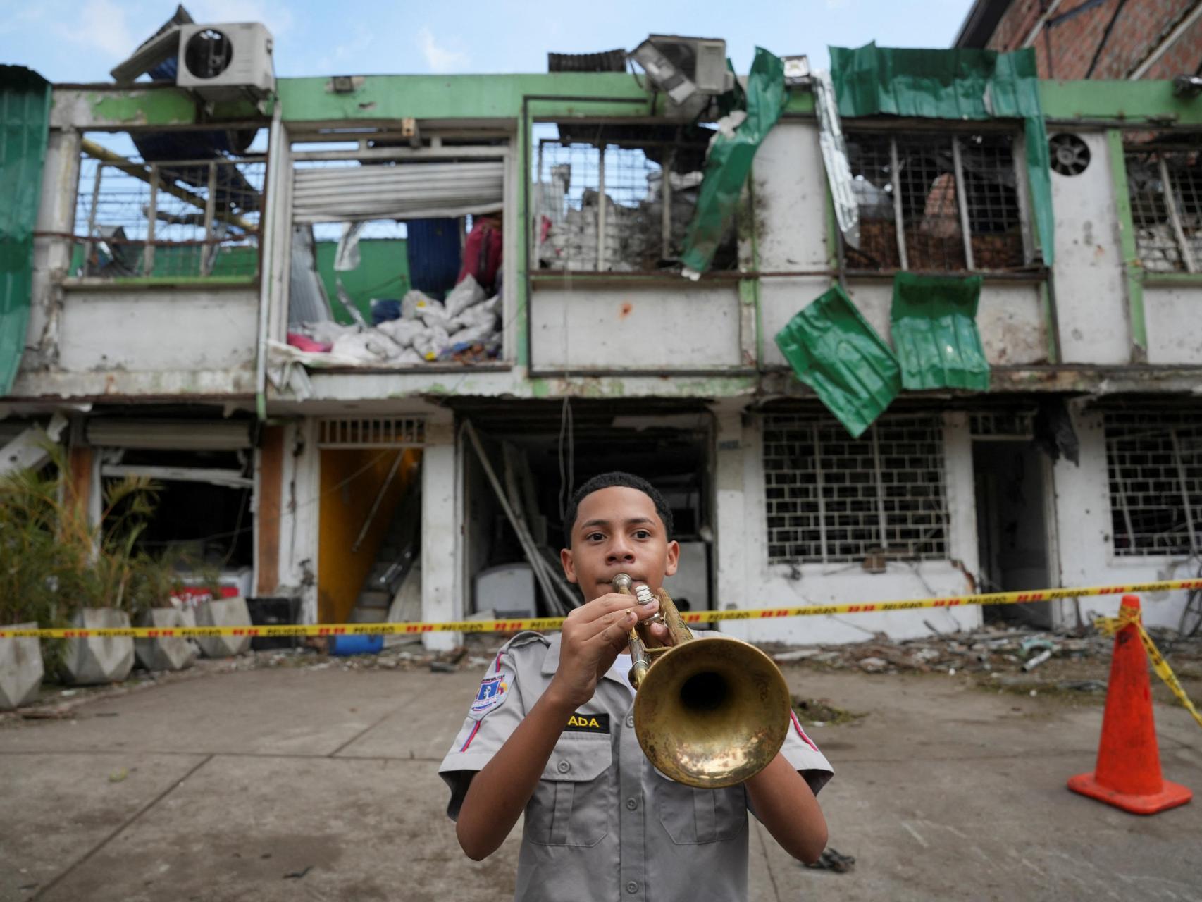 Un estudiante de una escuela secundaria militar toca la trompeta frente a un edificio dañado cerca de la base de la Fuerza Aeroespacial Colombiana, tras un atentado.