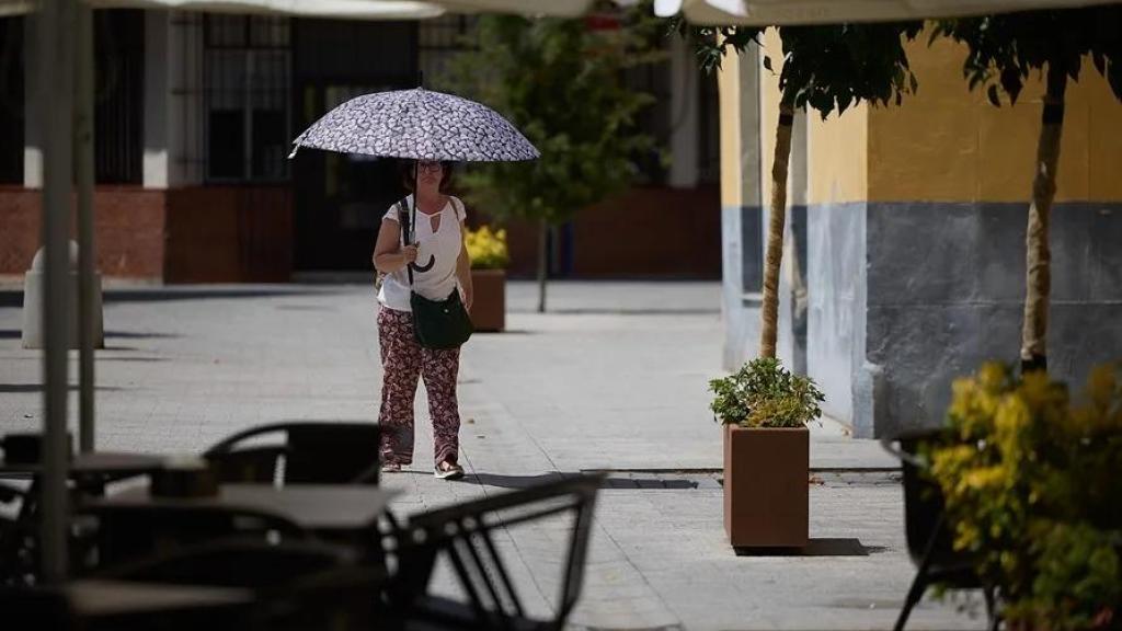 Una mujer se protege del sol con un paraguas cerca una terraza, en Talavera de la Reina.