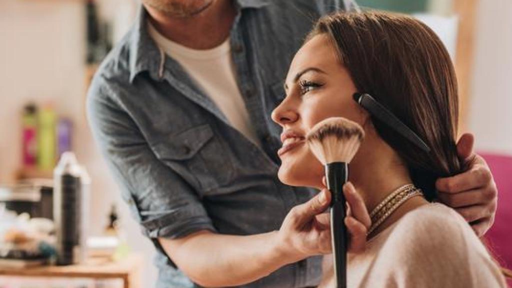 Maquillador aplicando colorete sobre una mujer.