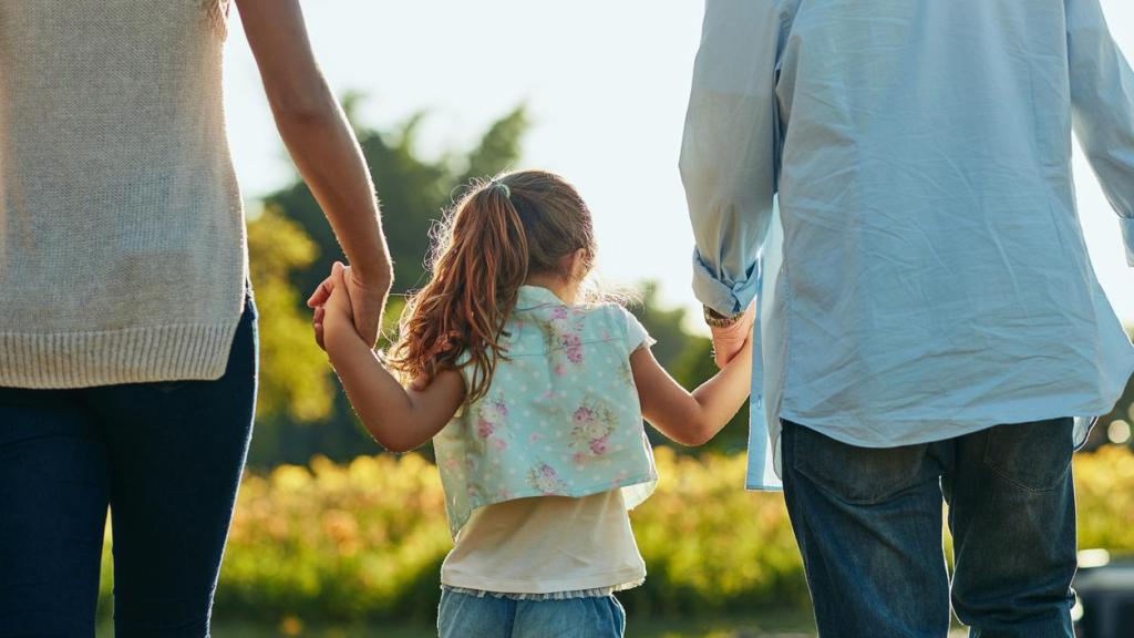 Imagen de archivo de una niña con sus progenitores de la mano.