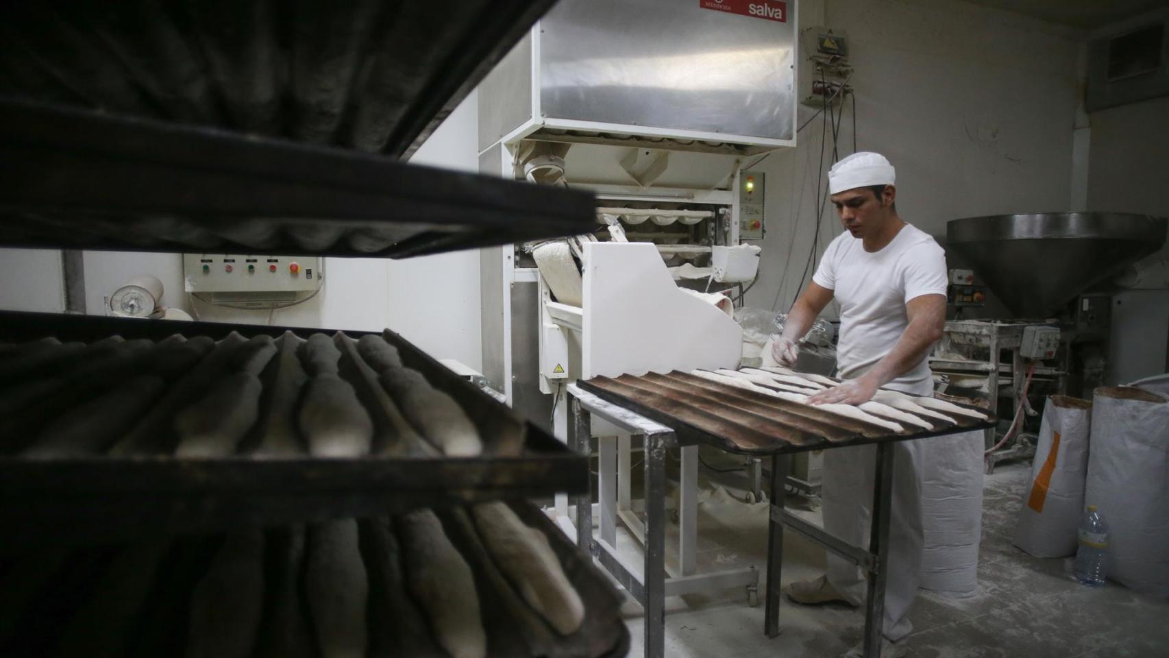 Un trabajador en un obrador preparando barras de pan.