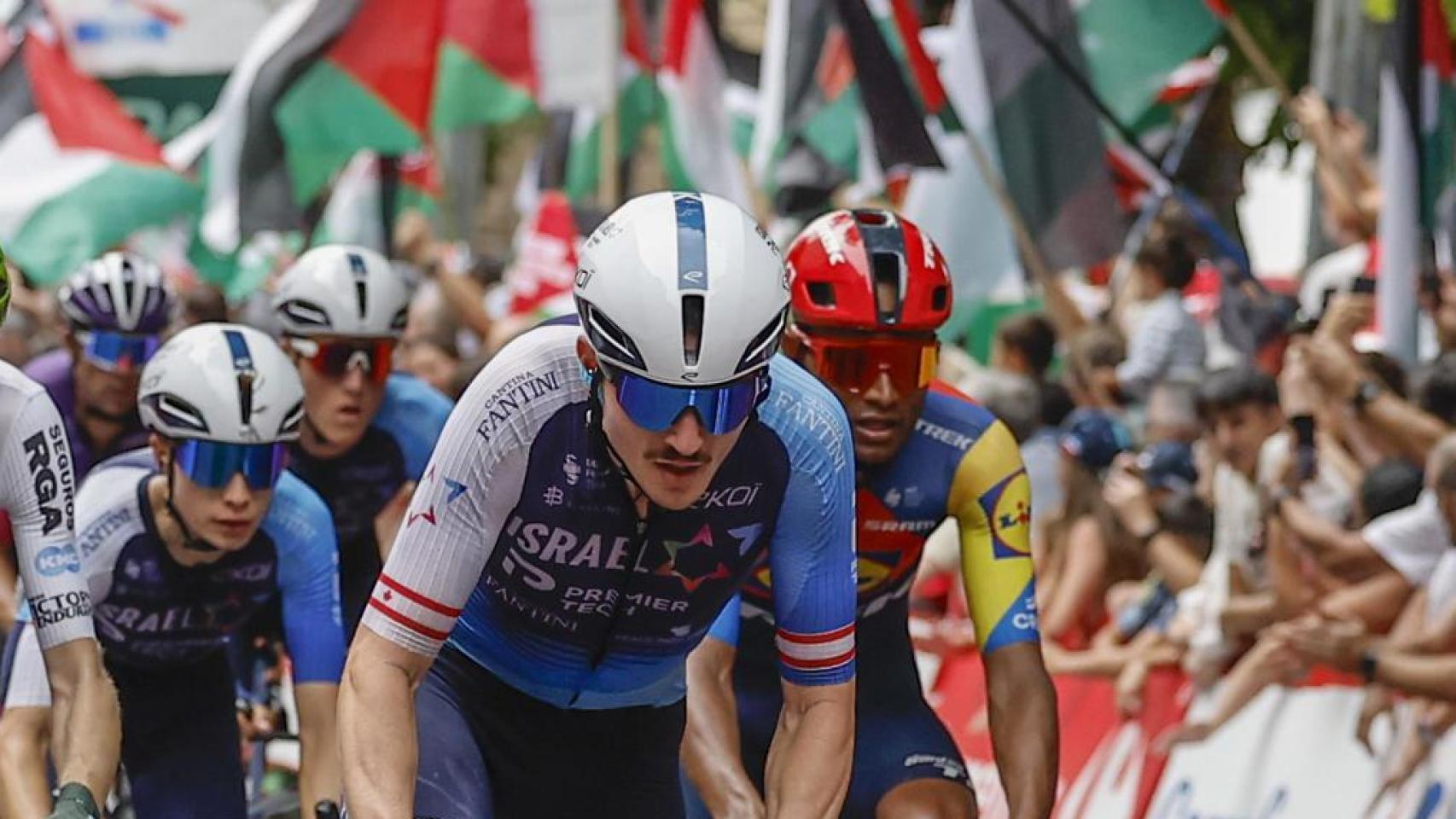 Un miembro del Israel Premier Tech en La Vuelta 2025 y, al fondo, una protesta propalestina
