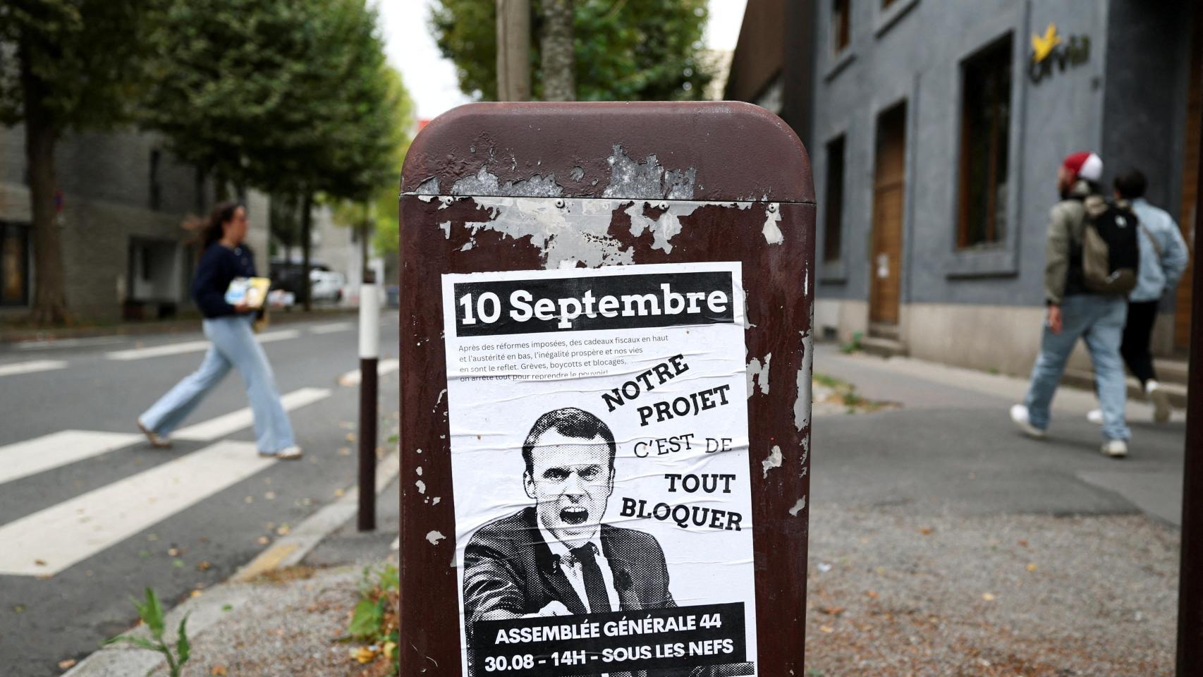 La gente pasa junto a un cartel que representa al presidente francés Emmanuel Macron con el lema Notre projet c'est de tout bloquer (Nuestro proyecto es bloquearlo todo).