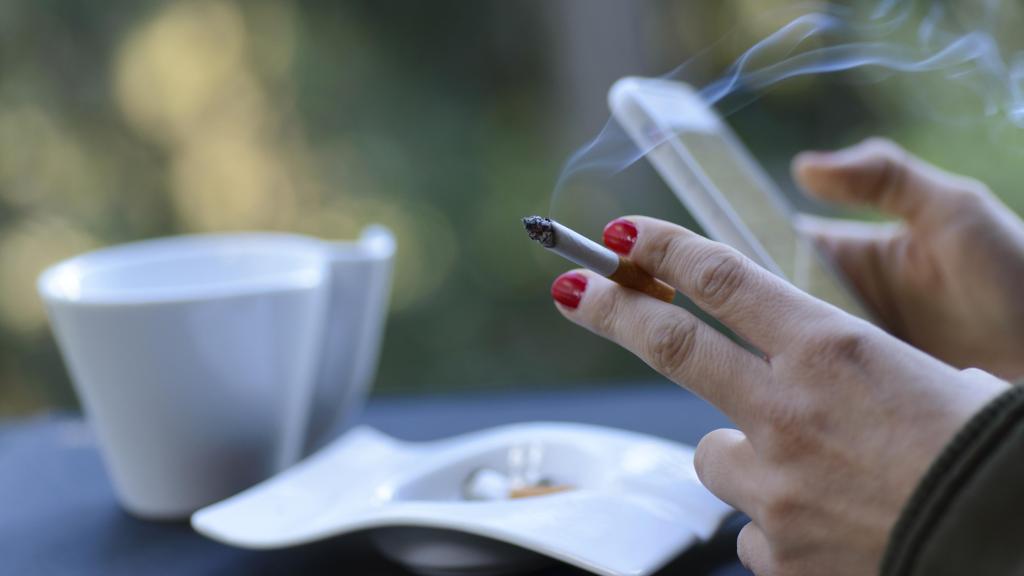 Una mujer fuma en una terraza mientras mira el móvil.