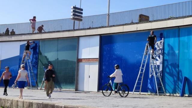Operarios, este martes, terminan de cubrir los Arcados de Riazor con vinilos con el escudo del Deportivo.