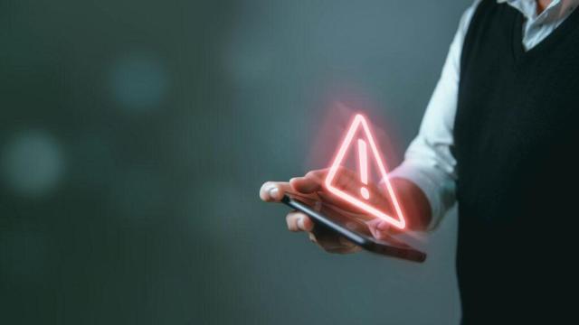 Imagen del símbolo de peligro sobre la pantalla de un teléfono móvil para ilustrar los riesgos en el mundo digital.