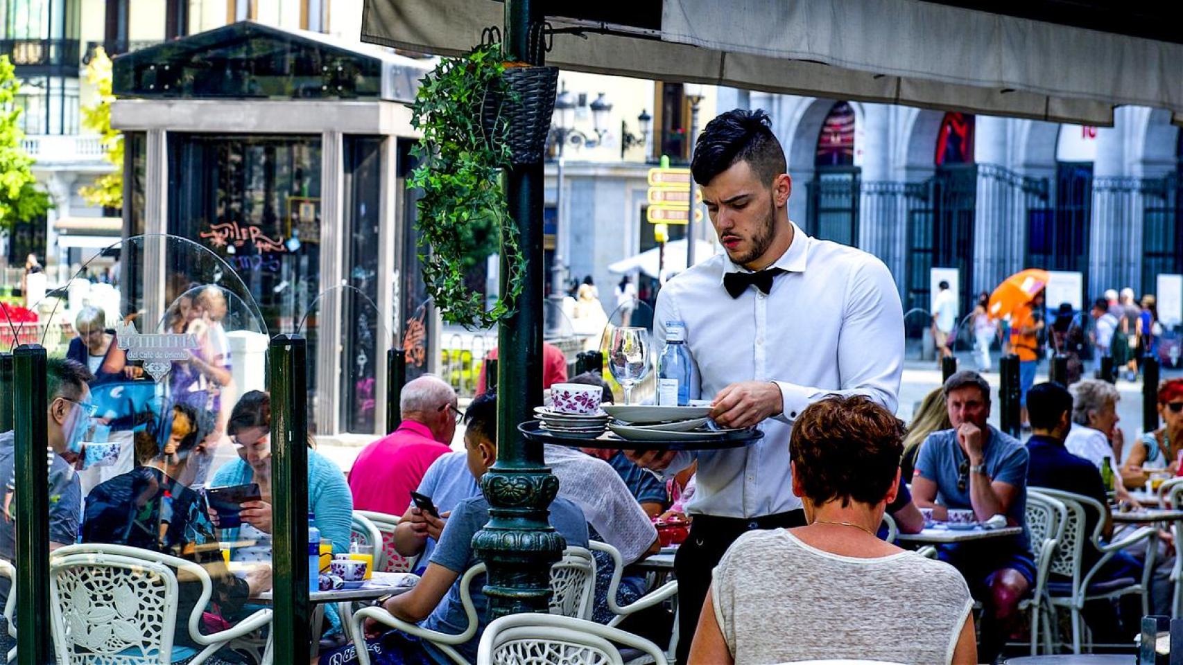 Camarero recogiendo los cubiertos y la cuenta de una mesa en una terraza de un café de Madrid.