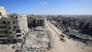 An image of Gaza City, with people walking through the rubble of buildings.