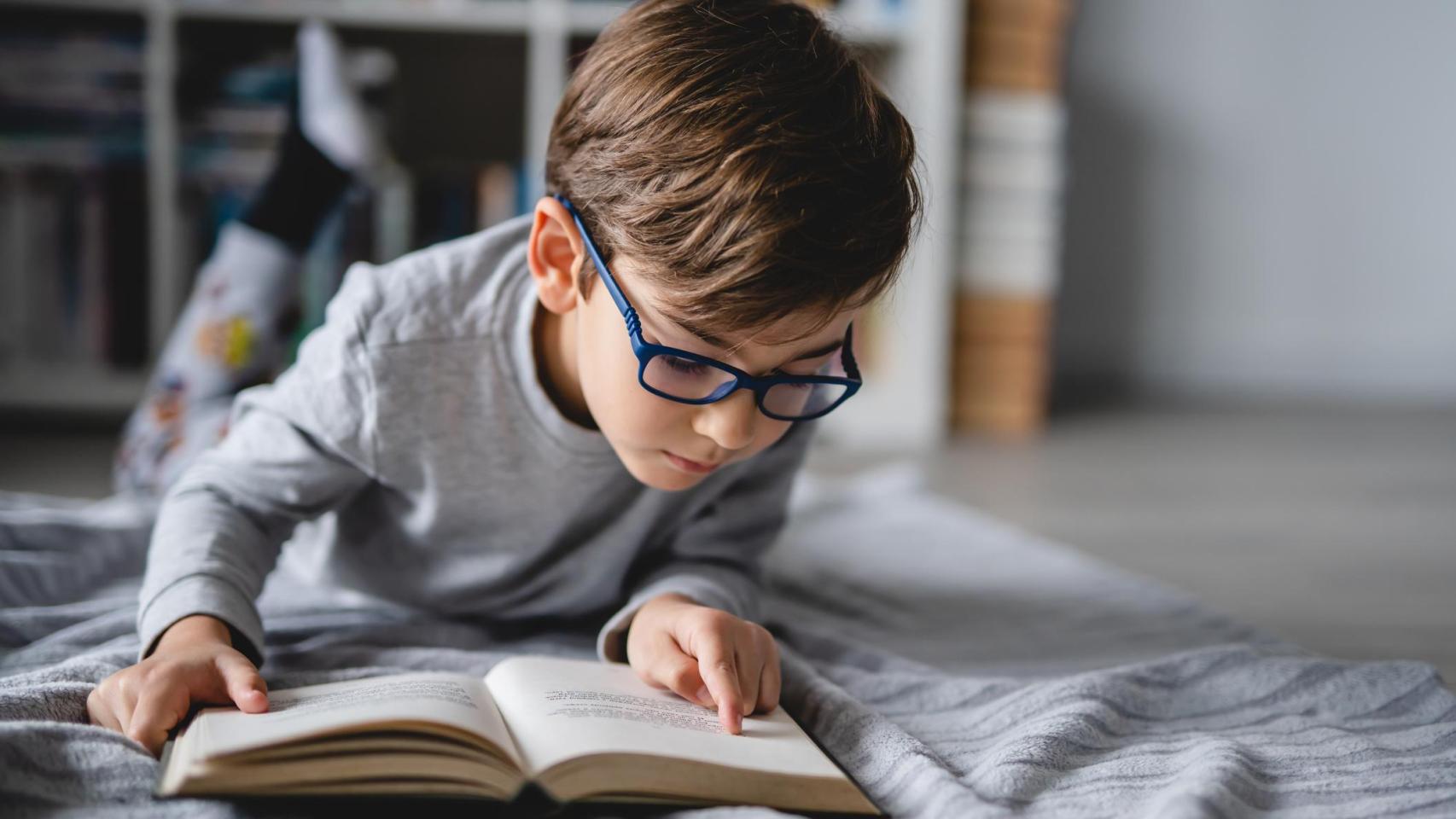 Un niño acostado en el suelo leyendo un libro.
