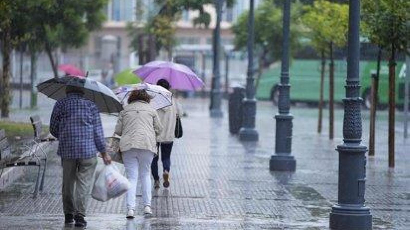 Personas andando por Sevilla bajo la lluvia.