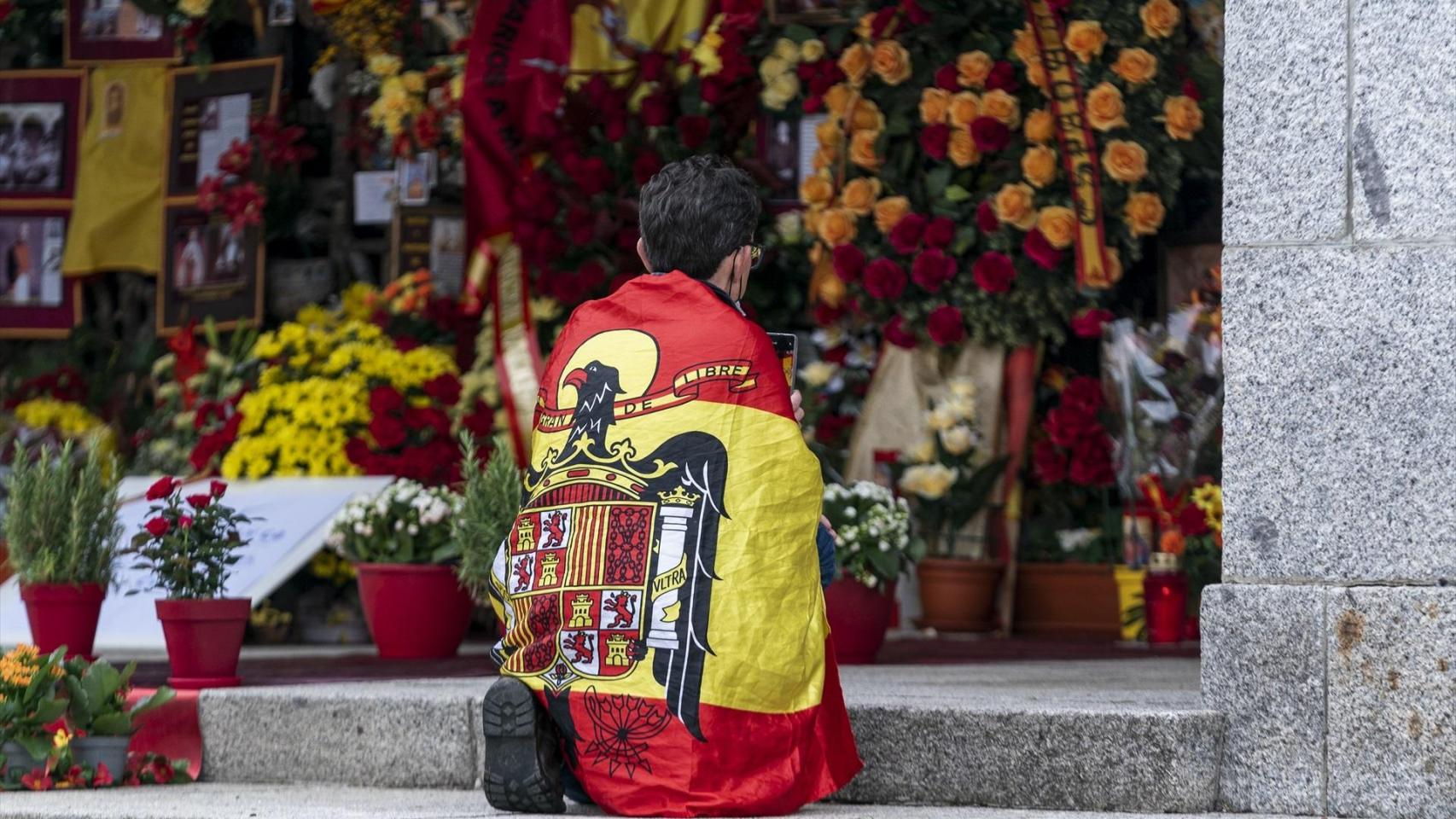 Un hombre envuelto en un abandera preconstitucional se arrodilla frente al panteón de la familia Franco.