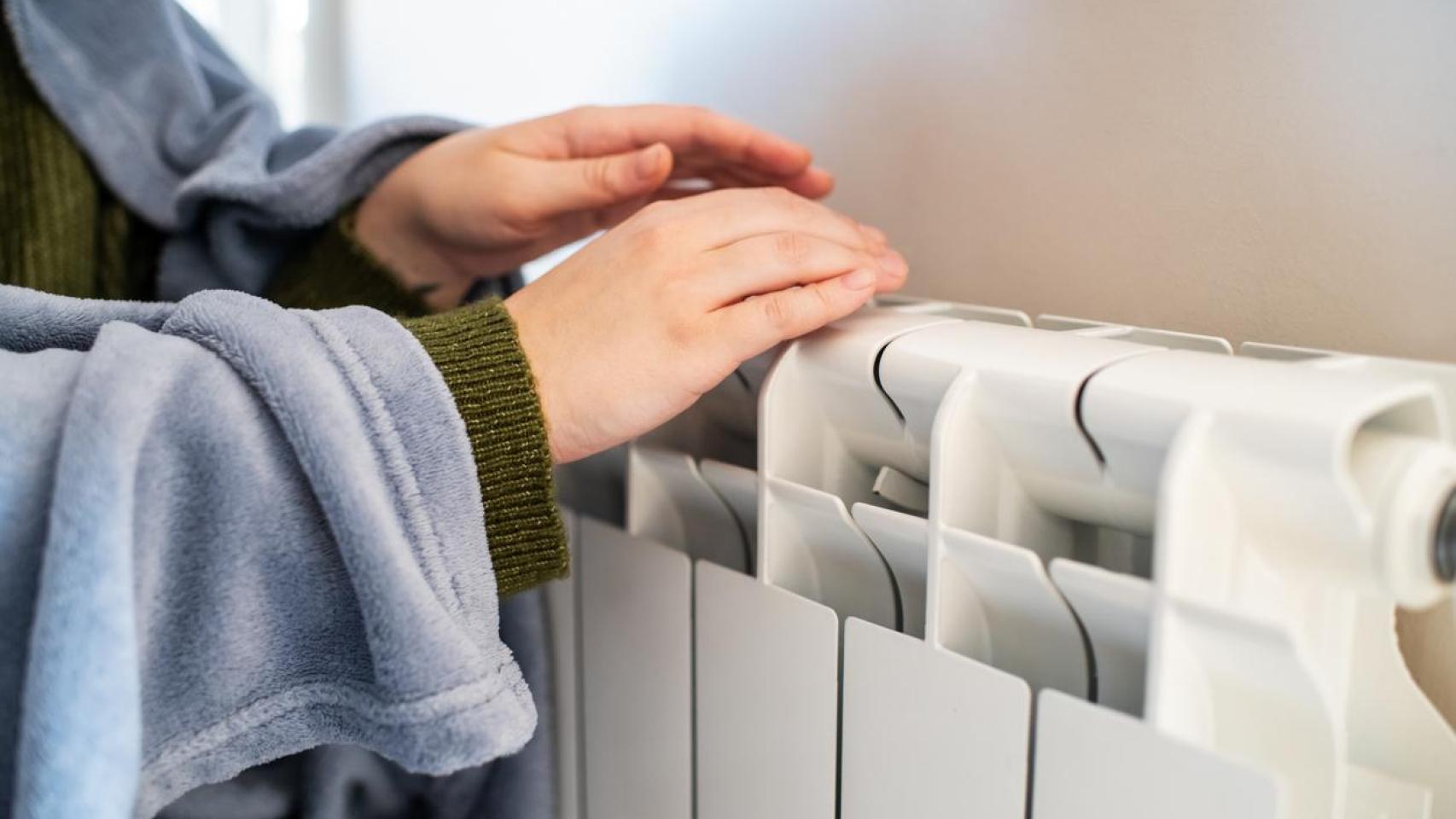 Una persona tratando de calentarse junto a un radiador.